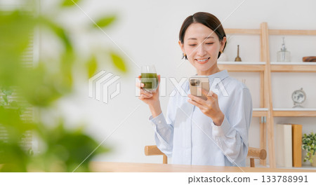 一名女子手拿綠色果汁和智慧型手機（橫幅） 133788991