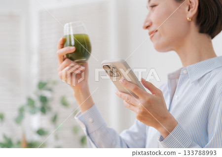 一位女士手捧綠色果汁和一部智慧型手機 133788993