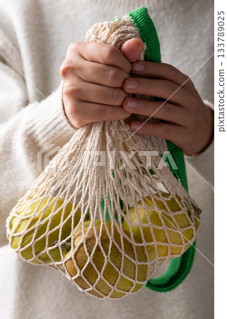 Fresh pear in mesh bag holding by woman hand 133789025