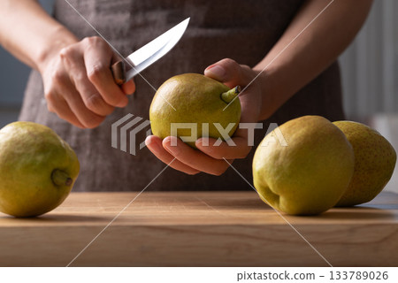 Hand holding kitchen knife and cutting pear on wooden board 133789026