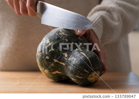 Hand holding kitchen knife and cutting green butternut squash on wooden board 133789047
