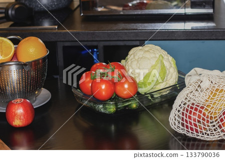 Fresh cucumbers and tomatoes laid out on a plate on the kitchen table, with fresh fruits and vegetables in the background. Useful ingredients for making salad at home. Fresh cucumbers and tomatoes laid out on a plate on the kitchen table, with fresh fruits and vegetables in the background. Useful ingredients for making salad at home. 133790036