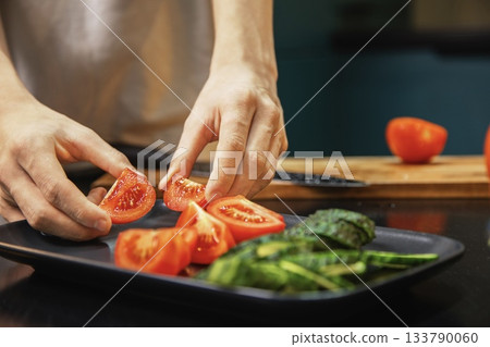 Person arranging sliced tomatoes and cucumbers on a plate while preparing a fresh salad in the kitchen. Healthy eating, fresh vegetables, and clean food preparation at home.  133790060