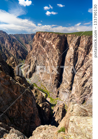 View of the massive Painted Wall in Black Canyon of the Gunnison National Park. White pegmatite dikes create stripes on the dark, sheer cliff. The Gunnison River is visible below 133790130