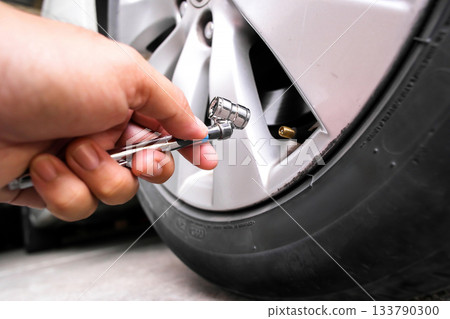Hand using a tire pressure gauge on a car valve stem 133790300