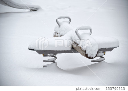 Snow-covered playground equipment in winter, a seesaw covered in snow Snow-covered playground equipment in winter, a seesaw covered in snow 133790313