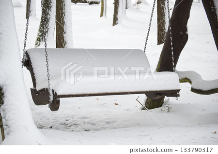 Snow-covered wooden swing in a winter wonderland forest scene Snow-covered wooden swing in a winter wonderland forest scene 133790317