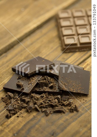 Dark chocolate squares with broken shards lying on wooden tabletop, showing segmented chocolate bar Dark chocolate squares with broken shards lying on wooden tabletop, showing segmented chocolate bar 133791049