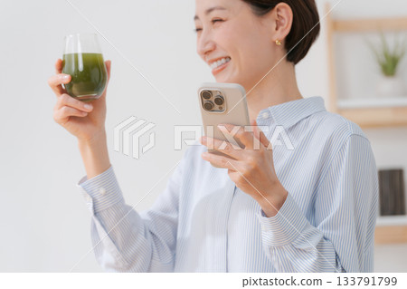 A woman with green juice and a smartphone 133791799