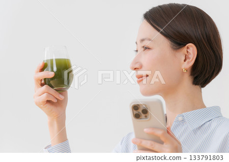 一位女士手捧綠色果汁和一部智慧型手機 133791803