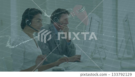 Call center agents monitoring financial overlay on screens at open-plan office desk, with headsets Call center agents monitoring financial overlay on screens at open-plan office desk, with headsets 133792129