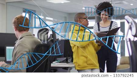 Reviewing notebook two colleagues standing in modern open-plan office, with dual monitors 133792245
