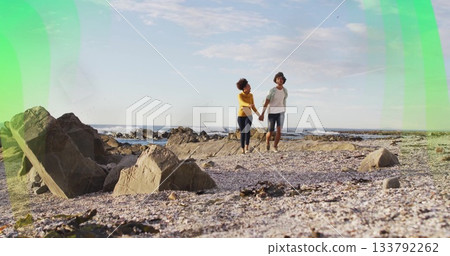 Walking man and woman holding hands on rocky shoreline, with pebbles shells ocean waves Walking man and woman holding hands on rocky shoreline, with pebbles shells ocean waves 133792262