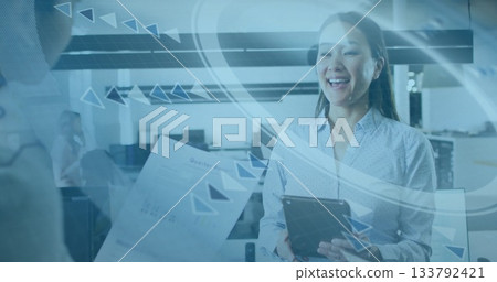 Smiling Korean woman holding tablet and receiving report in open office, with data graphics 133792421
