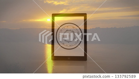 Tablet showing circular data image against serene sunset landscape backdrop 133792589