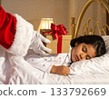 A child sleeps, eagerly waiting for a Christmas present. Santa Claus quietly places a present next to the child's pillow. 133792669