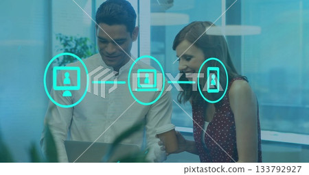 Collaborating male and female coworkers leaning on silver laptop in office with turquoise icons 133792927