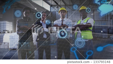 Collaborating team wearing yellow hard hats and vest studying holograms around pallets in warehouse 133793148