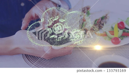 Holding smartphone projecting holographic cloud above dining table, with skewers and coffee cup 133793169