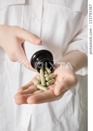 Person pouring dietary supplements or medicine into an open palm 133793367