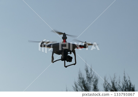 Drone with digital camera flying in the blue sky at sunset. Drone with digital camera flying in the blue sky at sunset. 133793867