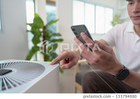 Technology and Lifestyle. Man controlling air purifier with smartphone. Technology and Lifestyle. Man controlling air purifier with smartphone. 133794880