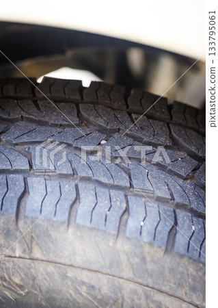 Closeup of a four-wheel drive pickup truck all-terrain tire showing worn tread patterns, dirt, and signs of rugged off-road use 133795061