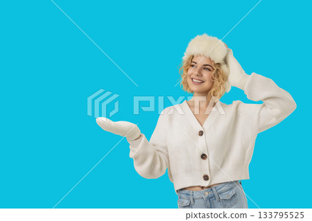 Woman wearing a cozy sweater and furry hat gesturing cheerfully 133795525