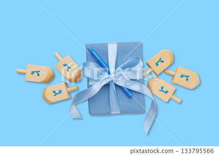 Hanukkah, blue gift box is surrounded by wooden dreidels and blue pen 133795566