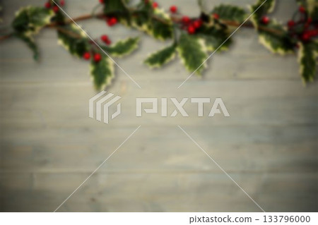 Variegated holly garland is draping across plank backdrop in flat design showing bright red berries 133796000