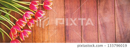Pink tulip blossoms with green stems are lying diagonally on warm wooden tabletop in flat design 133796019