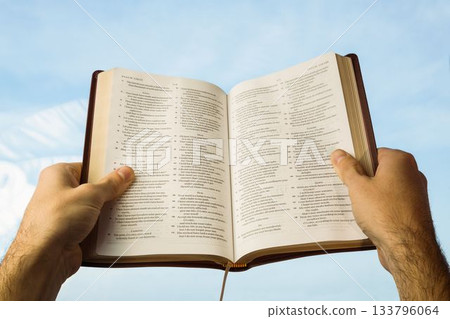 Close-up of hands holding open Bible against sky Close-up of hands holding open Bible against sky 133796064