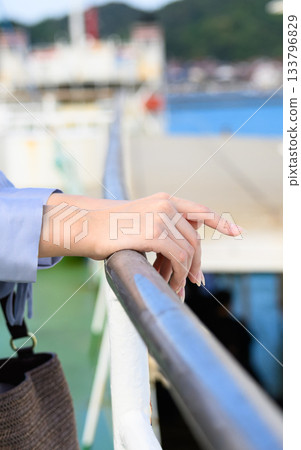 一隻女人的手撫摸著渡輪的欄桿，遠處是即將啟航的景象。 133796829
