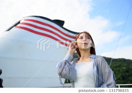 A young Japanese woman gazes into the future, with the blue sky reflected on the hull of a ferry 133796835