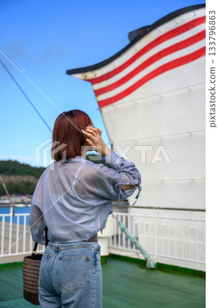 一位年輕女子背對著鏡頭,從渡輪甲板上眺望大海、島嶼、藍天和船體。 一位年輕女子背對著鏡頭,從渡輪甲板上眺望大海、島嶼、藍天和船體。 133796863
