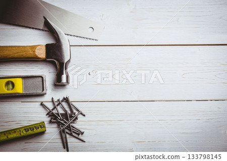 Saw blade, hammer, level, nails and tape are being arranged on painted white plank, copy space Saw blade, hammer, level, nails and tape are being arranged on painted white plank, copy space 133798145