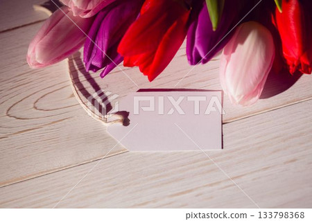 Tulip cluster is casting soft shadows on wooden tabletop in flat design, with blank gift tag 133798368