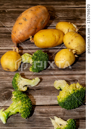 A mix of fresh raw produce, including potatoes, a sweet potato and broccoli florets sit on a rustic wooden surface, ready to be cooked. A mix of fresh raw produce, including potatoes, a sweet potato and broccoli florets sit on a rustic wooden surface, ready to be cooked. 133798670
