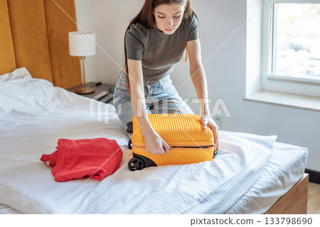 Woman packing suitcase on bed preparing for travel Woman packing suitcase on bed preparing for travel 133798690