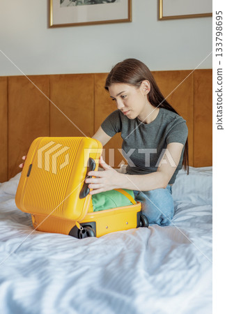 Young woman packing yellow suitcase on hotel bed Young woman packing yellow suitcase on hotel bed 133798695