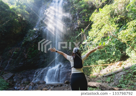 Woman with Outstretched Arms Embracing Nature at Majestic Waterfall Surrounded by Lush Greenery in Serene Outdoor Environment 133798792