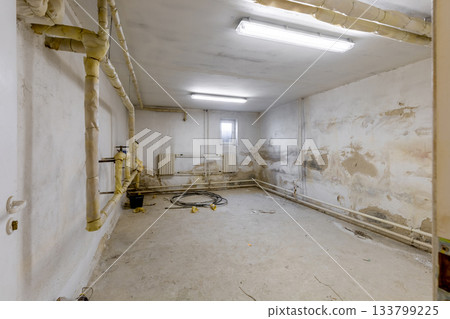Old Basement Room with Worn Walls and Heating Pipes 133799225