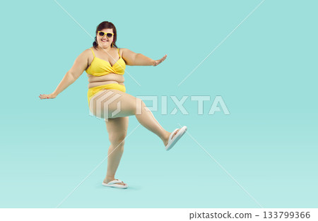 Funny young fat woman in yellow bikini and sunglasses having fun isolated on blue background. 133799366