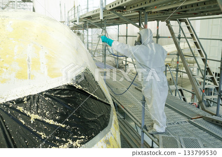 Worker applies protective coating on aircraft fuselage in hangar during maintenance process to prepare for future flights 133799530