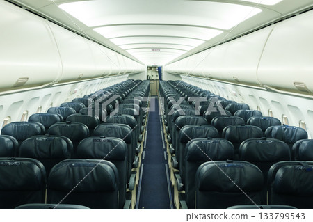 Empty airplane interior with rows of seats and dim lighting showing a quiet cabin atmosphere 133799543