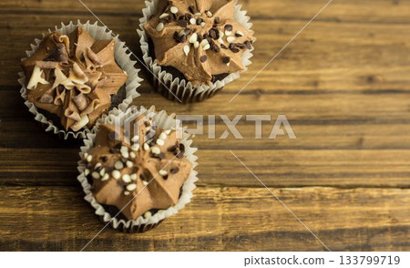 Flat design is showing three chocolate cupcakes with swirled frosting and sprinkles on wooden table 133799719