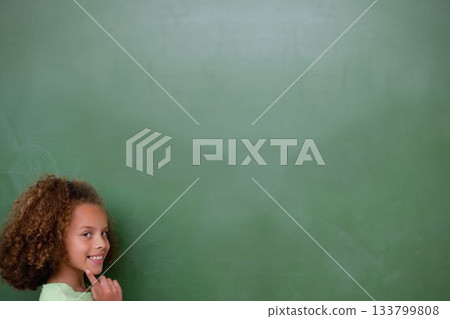 Smiling schoolgirl is standing before full-wall green chalkboard in flat design, copy space 133799808