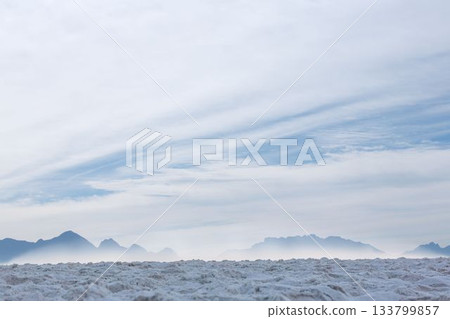 Flat design salt flat is stretching toward misty mountain ridge under wispy cloud layers Flat design salt flat is stretching toward misty mountain ridge under wispy cloud layers 133799857