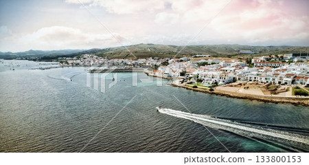 Speedboat is cutting through bay water in flat design with white red roofed houses, moored boats 133800153