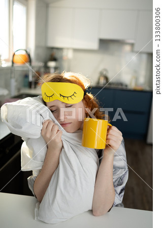 relaxed female enjoying slow morning coffee while wearing sleep accessories in kitchen relaxed female enjoying slow morning coffee while wearing sleep accessories in kitchen 133800306
